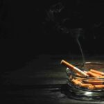 Smouldering cigarette in a glass ashtray on a dark table